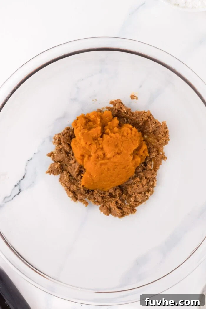 Almond butter mixed with brown sugar in a glass mixing bowl with a scoop of pumpkin puree on top.