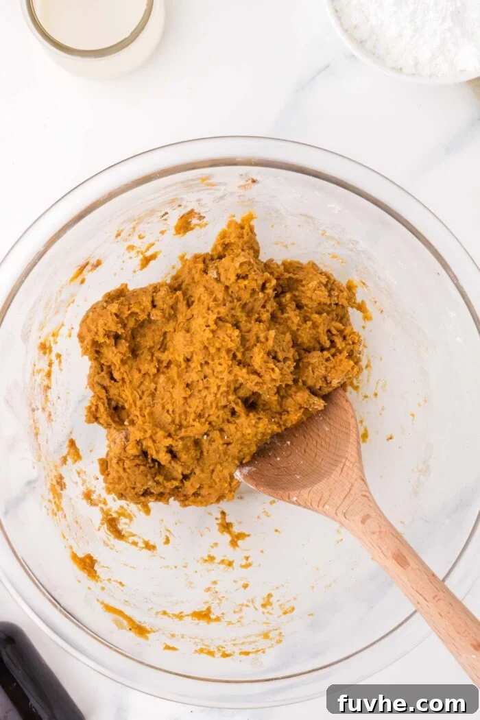 Vegan pumpkin cookie dough in a glass mixing bowl with a wooden spoon resting in the bowl.