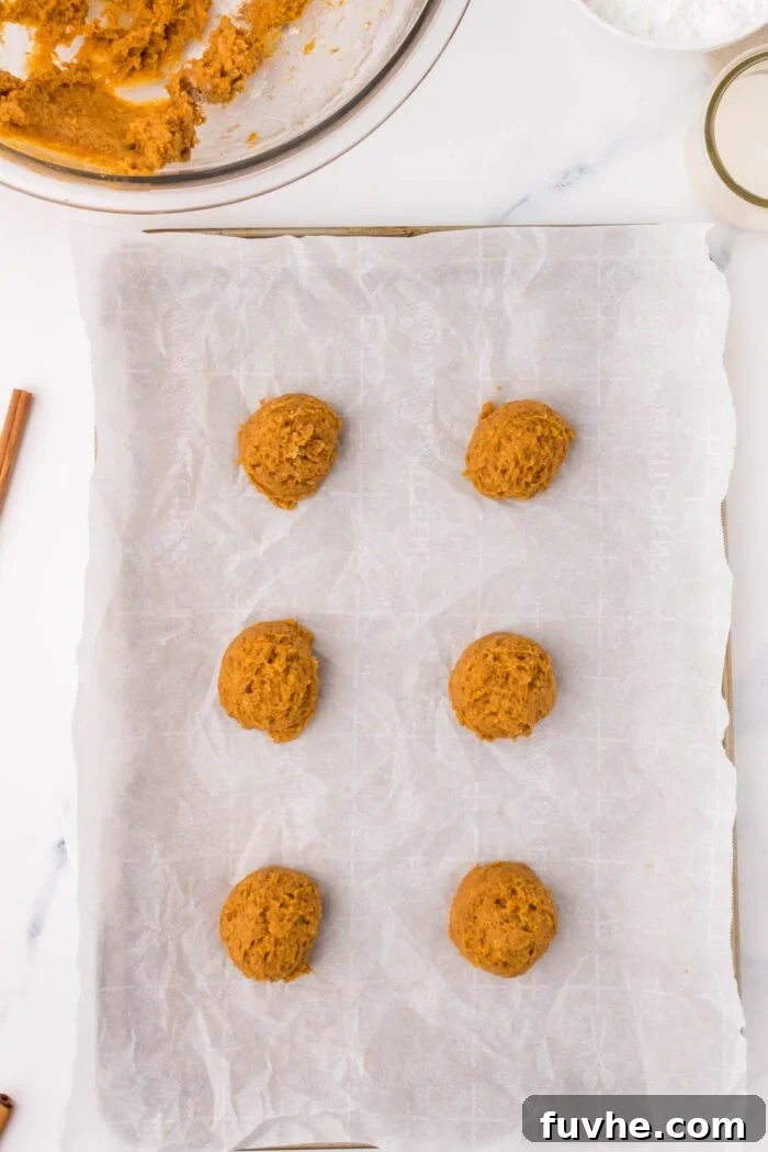 6 unbaked scoops of pumpkin cookie dough on a parchment paper-lined baking tray.