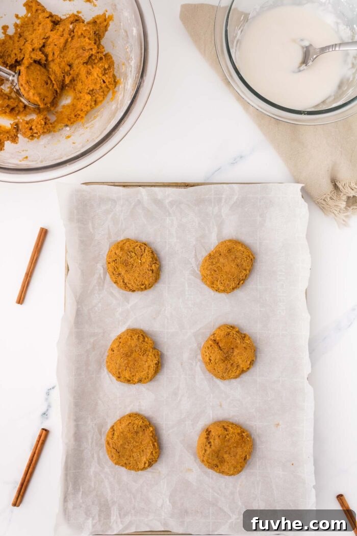 6 baked soft pumpkin cookies on a parchment-paper lined baking tray with a glass mixing bowl of cookie dough beside the tray.