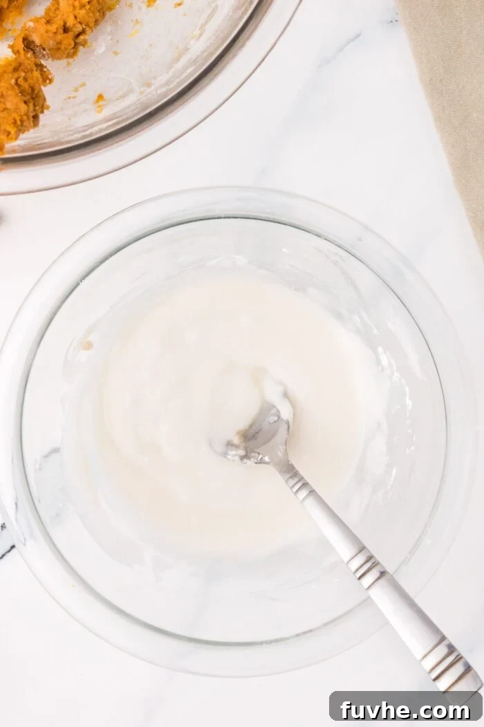 Powdered sugar glaze in a glass mixing bowl with a spoon.
