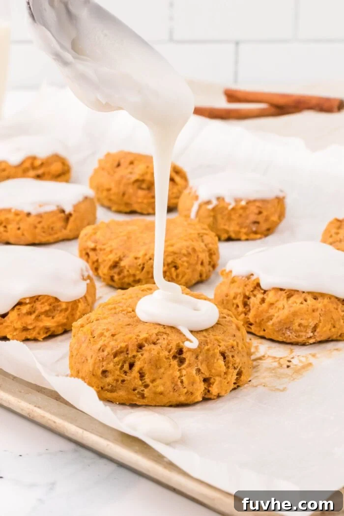 Drizzling powdered sugar icing over soft pumpkin cookies on a parchment paper-lined baking tray.