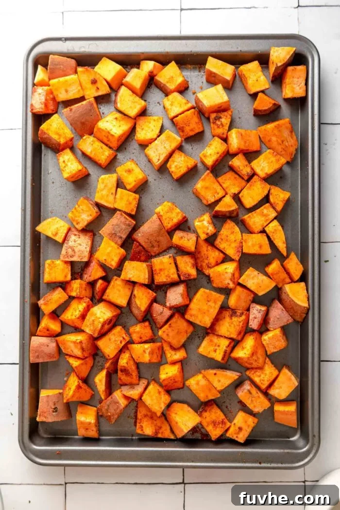 Spiced Sweet Potato and Black Bean Tacos 5 Cubed sweet potatoes, glistening with oil and generously coated in a mix of taco spices, spread evenly across a baking tray, ready for roasting.