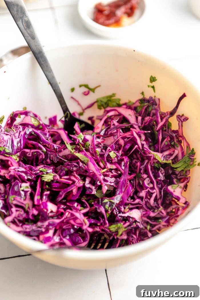 Spiced Sweet Potato and Black Bean Tacos 6 A vibrant red cabbage and cilantro slaw sits in a mixing bowl, ready to be served. A spoon and fork rest inside the bowl, highlighting its fresh appeal.