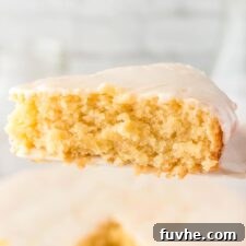 A slice of vegan olive oil cake topped with powdered sugar glaze held on a spatula over the whole cake below it.