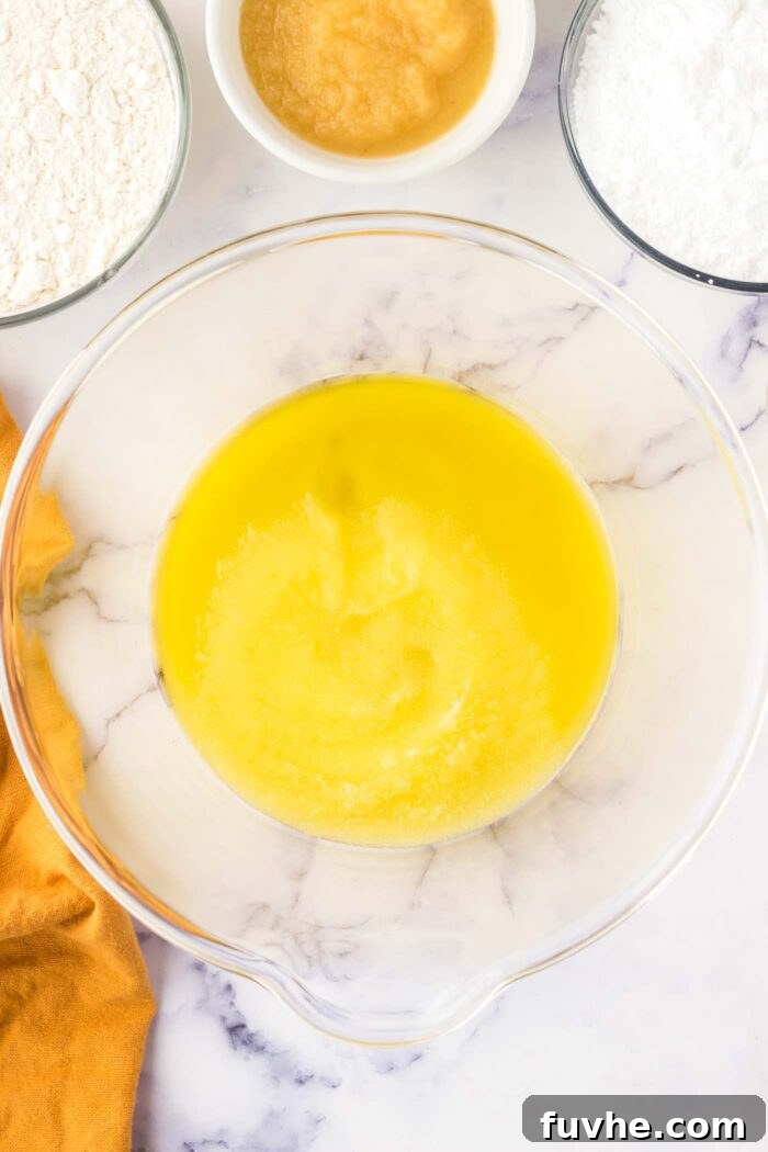 Olive oil and granulated sugar are creamed together in a large transparent glass mixing bowl, illustrating the initial step of the cake recipe.