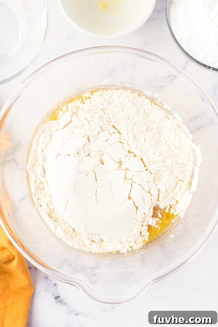 All-purpose flour, sea salt, and baking powder are carefully sifted over the wet olive oil cake mixture in a large glass mixing bowl.