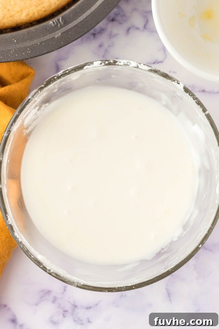A creamy, white lemon-flavored powdered sugar glaze is freshly mixed in a clear glass bowl, ready to be applied to a cake.