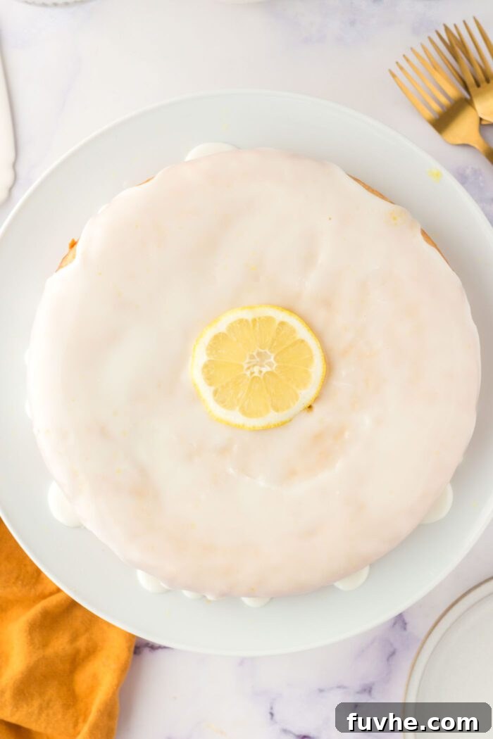 An overhead view of a beautifully glazed olive oil cake, adorned with a delicate slice of lemon in the center, presented on a elegant cake stand.
