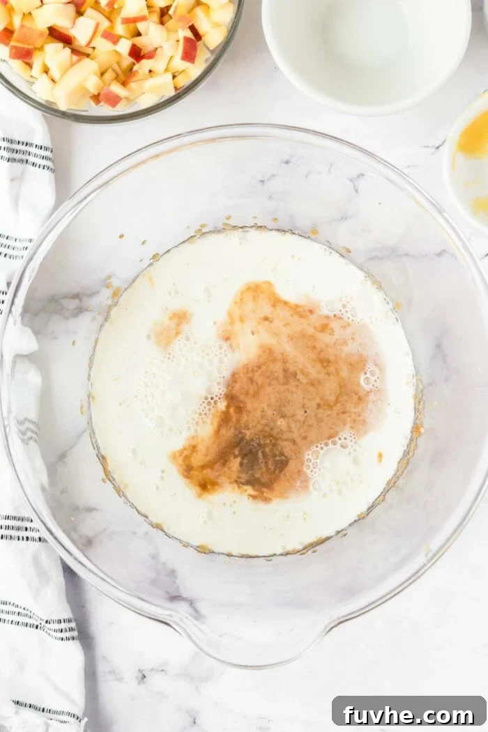 Vanilla and milk added to a glass mixing bowl with applesauce and sugar.