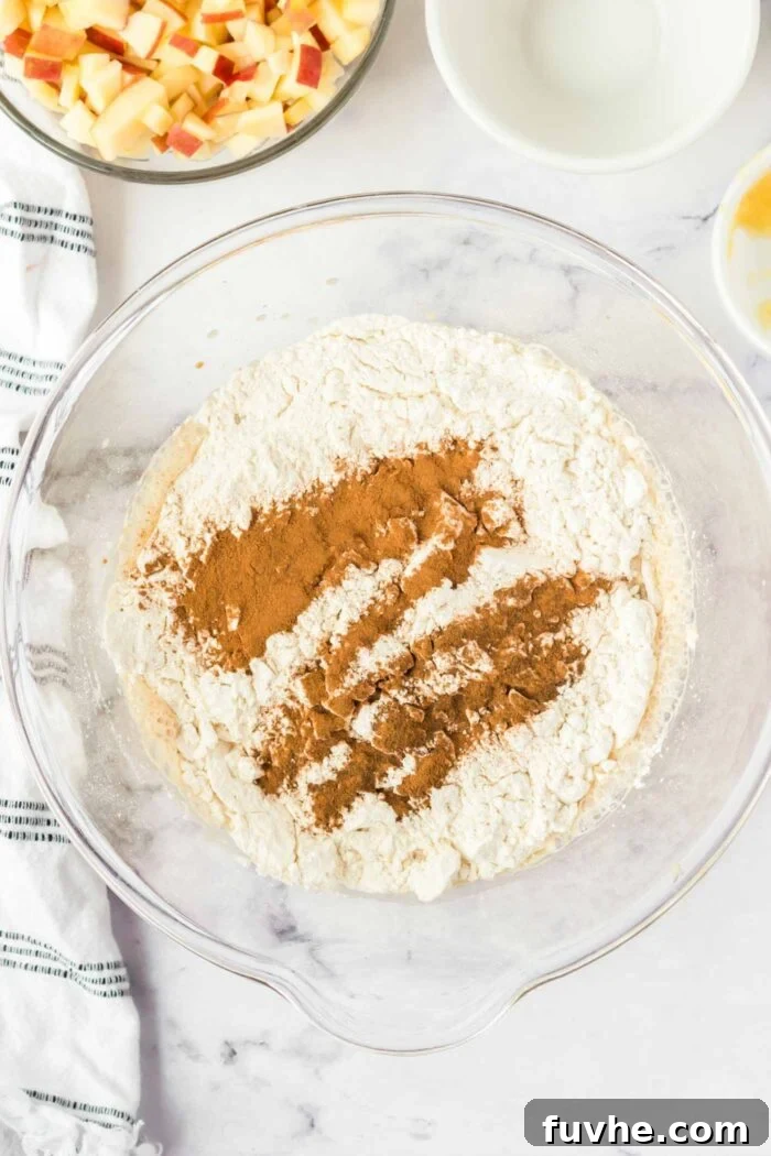 Flour, cinnamon and baking powder added to a glass mixing bowl with cake batter in it.