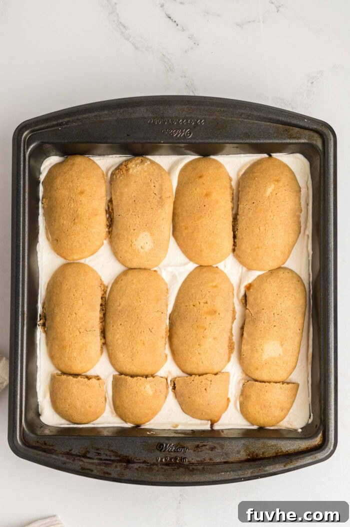 Decadent Vegan Tiramisu 18 A layer of golden brown ladyfinger cookies on a layer of creamy marscapone in a square baking pan.