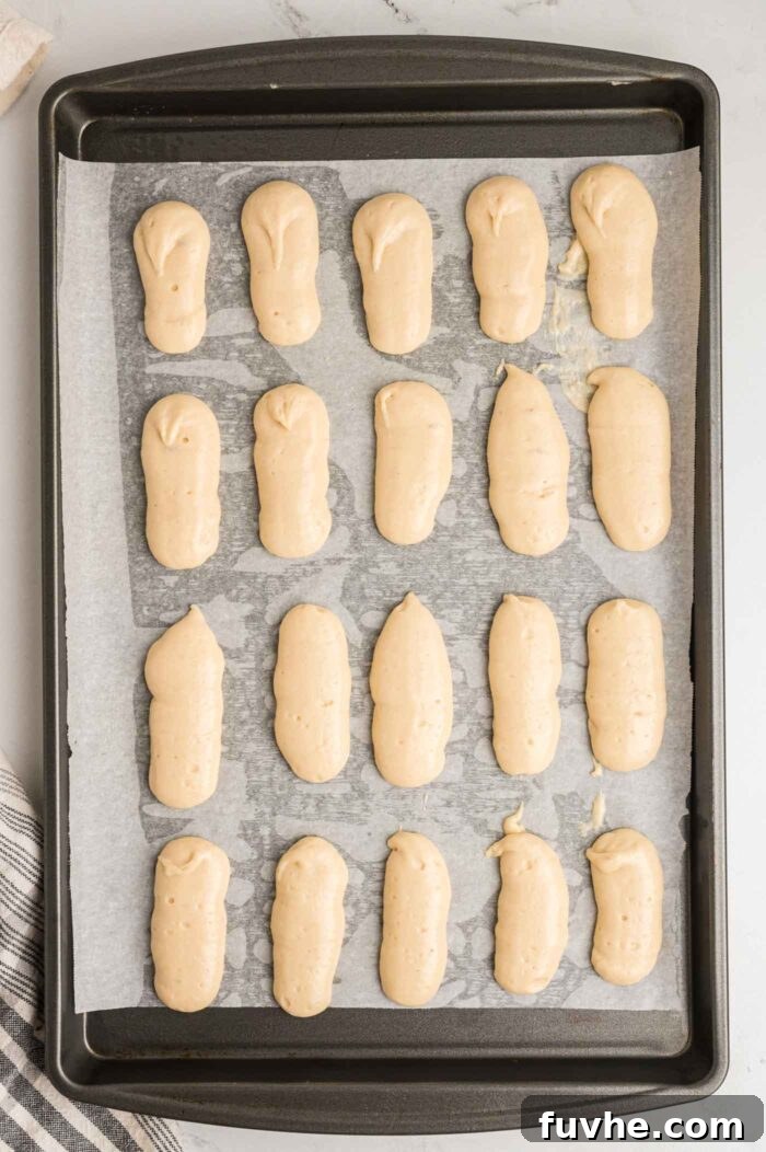 Decadent Vegan Tiramisu 10 20 raw ladyfingers piped onto a baking tray lined with parchment paper.