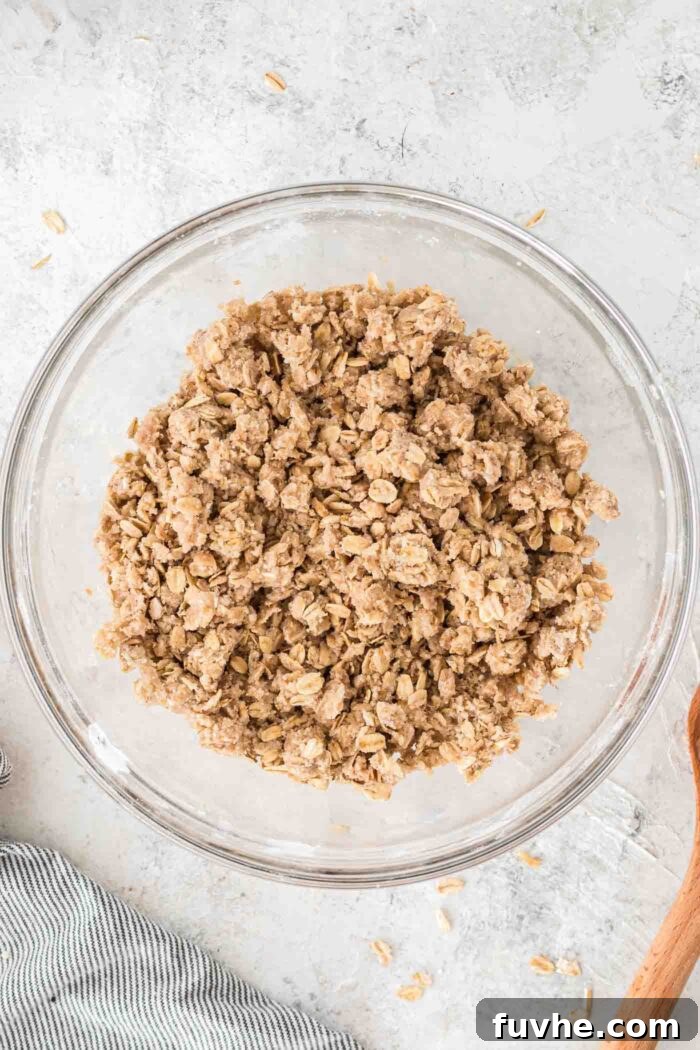 Irresistible Vegan Strawberry Crumble Bars 4 A glass mixing bowl filled with a raw oatmeal crumble mixture, featuring oats, brown sugar, and flour, ready for baking.