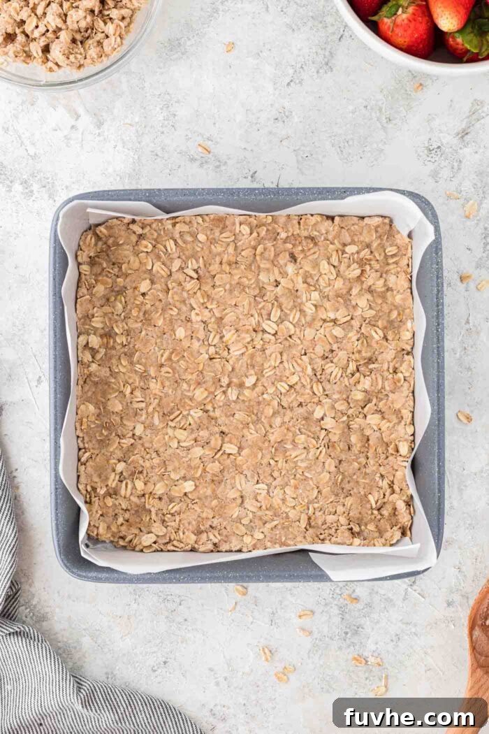 Irresistible Vegan Strawberry Crumble Bars 5 A golden-brown oatmeal crust pressed firmly into the bottom of a square baking pan, which is lined with parchment paper.
