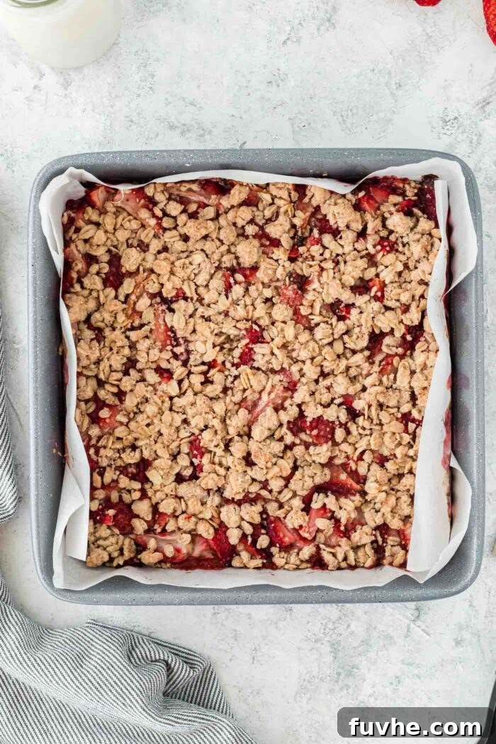 Irresistible Vegan Strawberry Crumble Bars 8 An overhead view of a square baking pan filled with unbaked strawberry oat bars, with the crumble topping spread over the strawberry layer, ready to be baked.