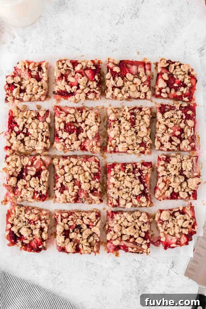 Irresistible Vegan Strawberry Crumble Bars 9 Sixteen perfectly cut vegan strawberry oatmeal bars arranged on a piece of parchment paper, with a knife resting alongside them.