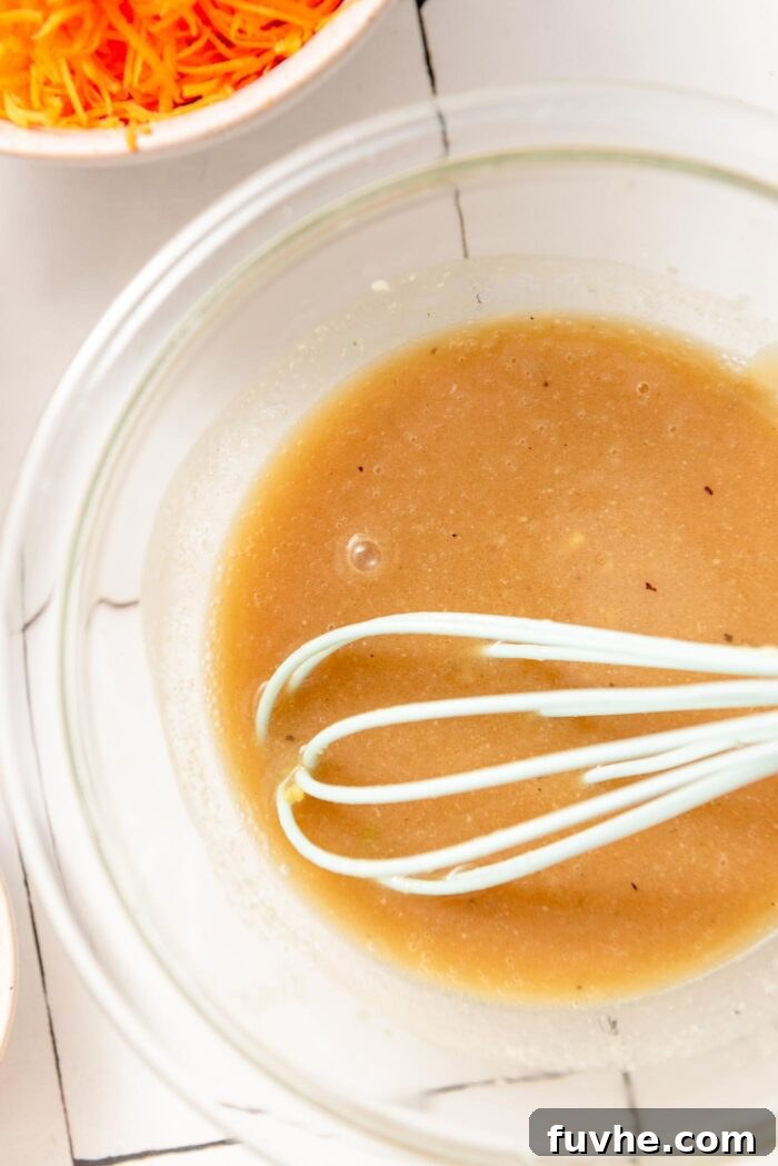 A small glass bowl containing a freshly mixed sesame salad dressing, with a whisk resting inside, showing its smooth and creamy texture.