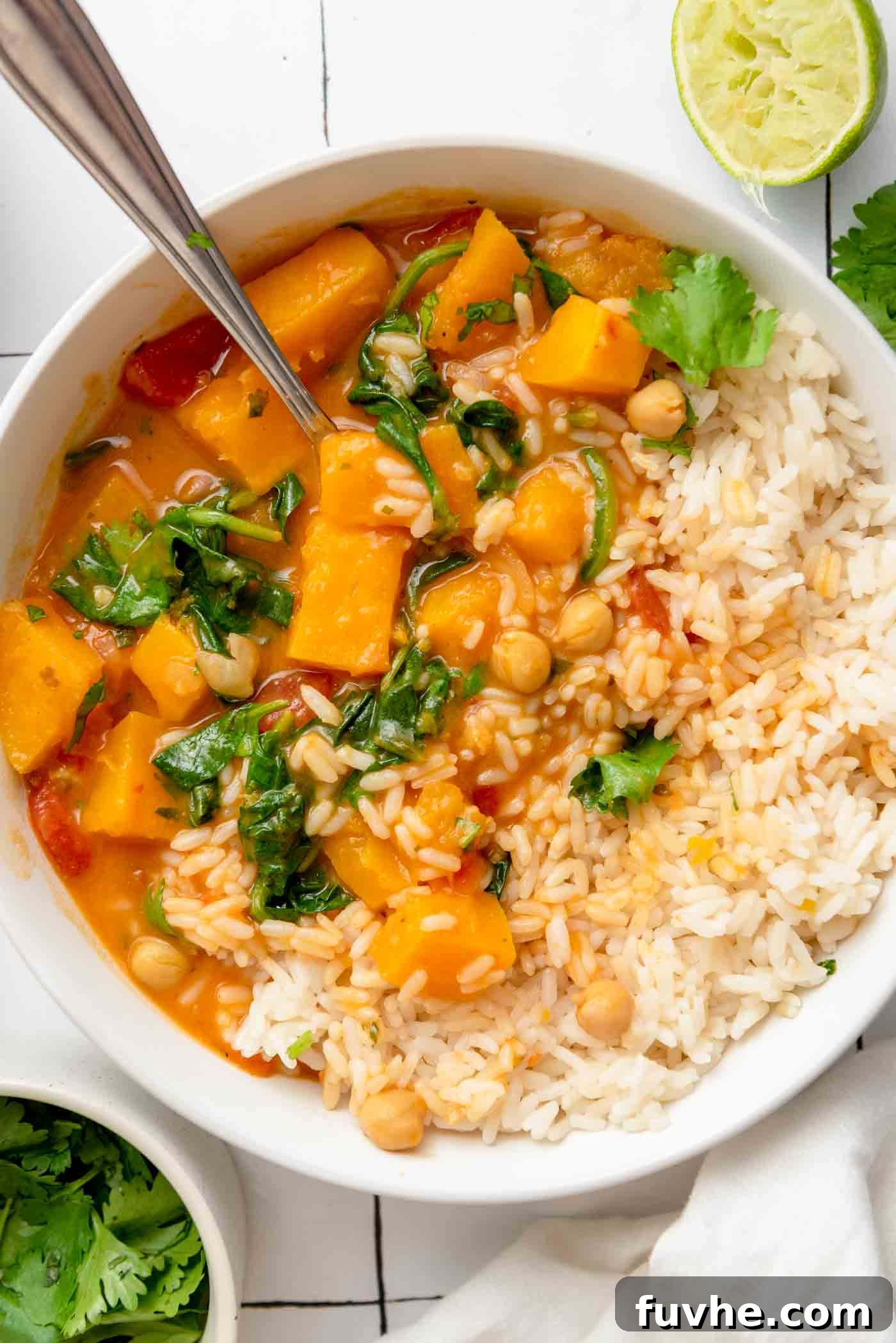 Bowl of creamy butternut squash curry with chickpeas and spinach served with rice, garnished with fresh cilantro.