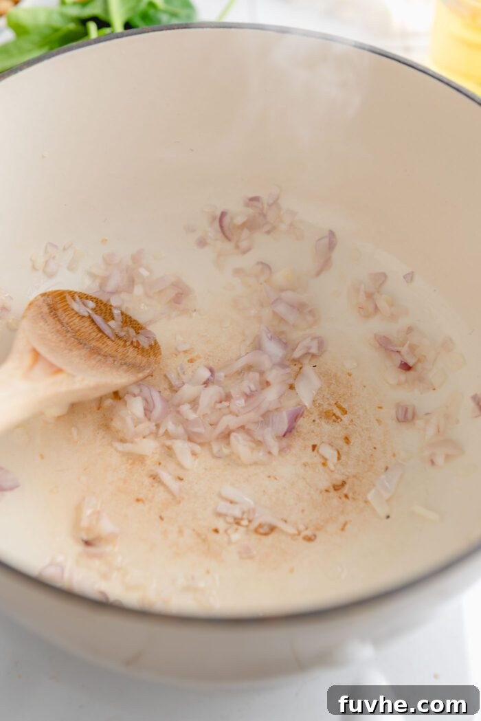 Finely minced shallot cooking gently in a large soup pot with a wooden spoon, releasing its wonderfully fragrant aroma as it softens.
