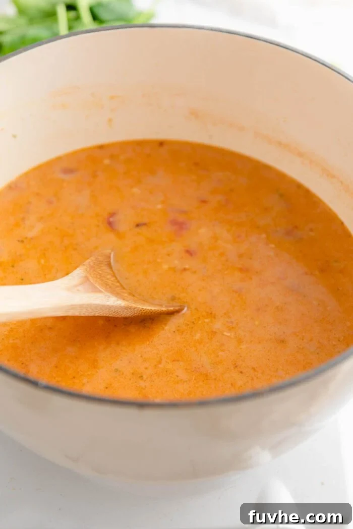 A creamy red curry sauce simmering gently in a large Dutch oven with a wooden spoon, gradually thickening to a luscious consistency.