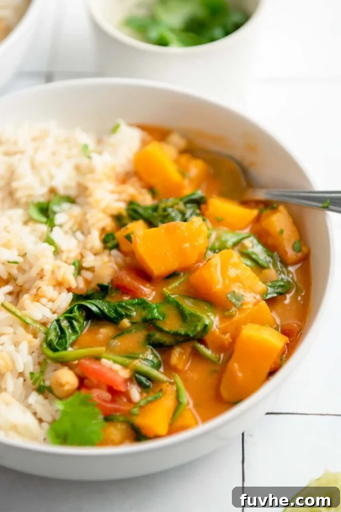 A warm, inviting bowl of roasted butternut squash curry with spinach and chickpeas, served with a generous side of fluffy white rice, ready to be enjoyed.
