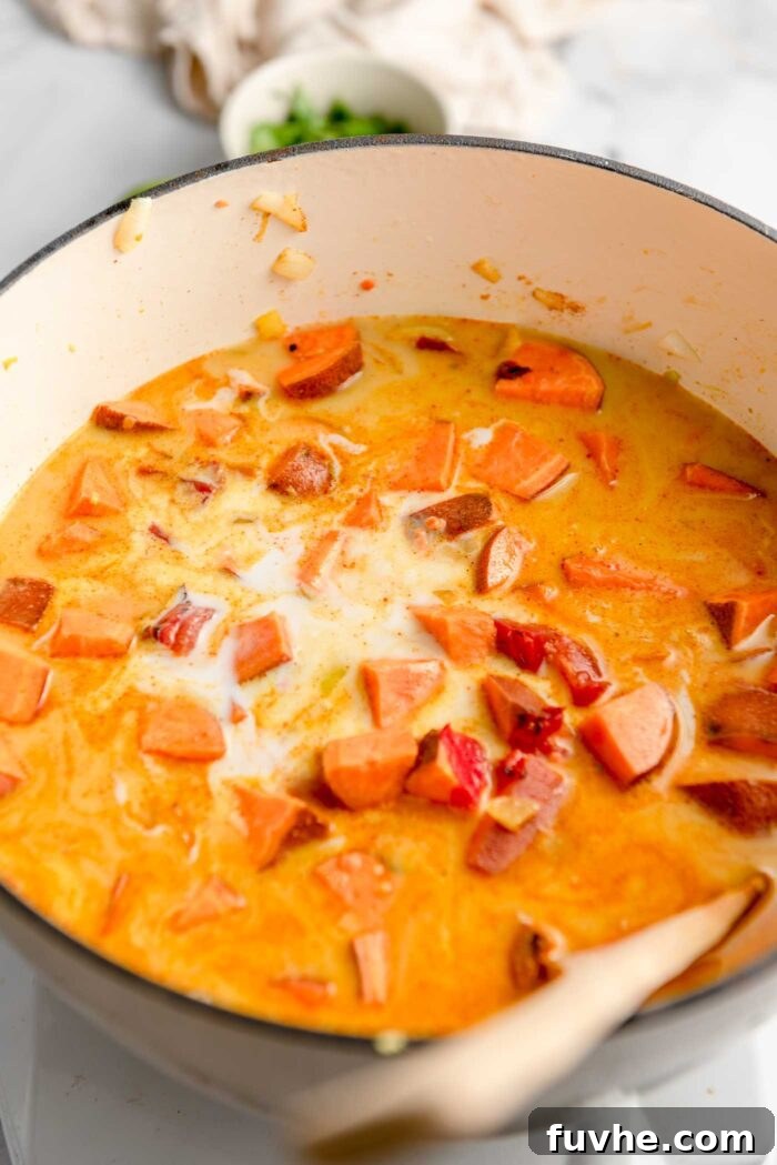 A large pot on the stovetop filled with coconut milk, diced tomatoes, sweet potatoes, and broth, gently simmering to create the rich curry.