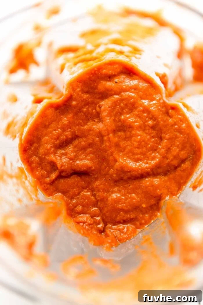 A creamy red sauce made from chipotle peppers, roasted poblano, onion, and tomato paste, ready to be poured over the tofu in a blender.