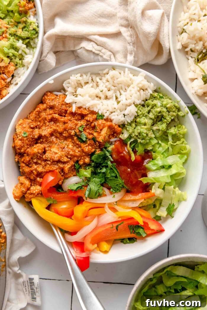 Overhead view of a vibrant tofu sofritas burrito bowl filled with cilantro lime rice, fresh guacamole, chopped cilantro, crisp lettuce, and tender cooked peppers and onions.