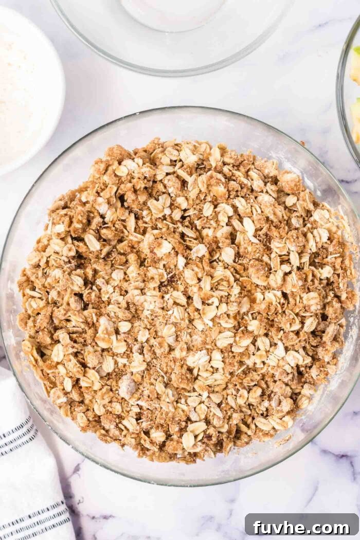 A glass mixing bowl holds a mixture of oatmeal, brown sugar, melted butter, and flour, ready to be transformed into a delicious crumble.