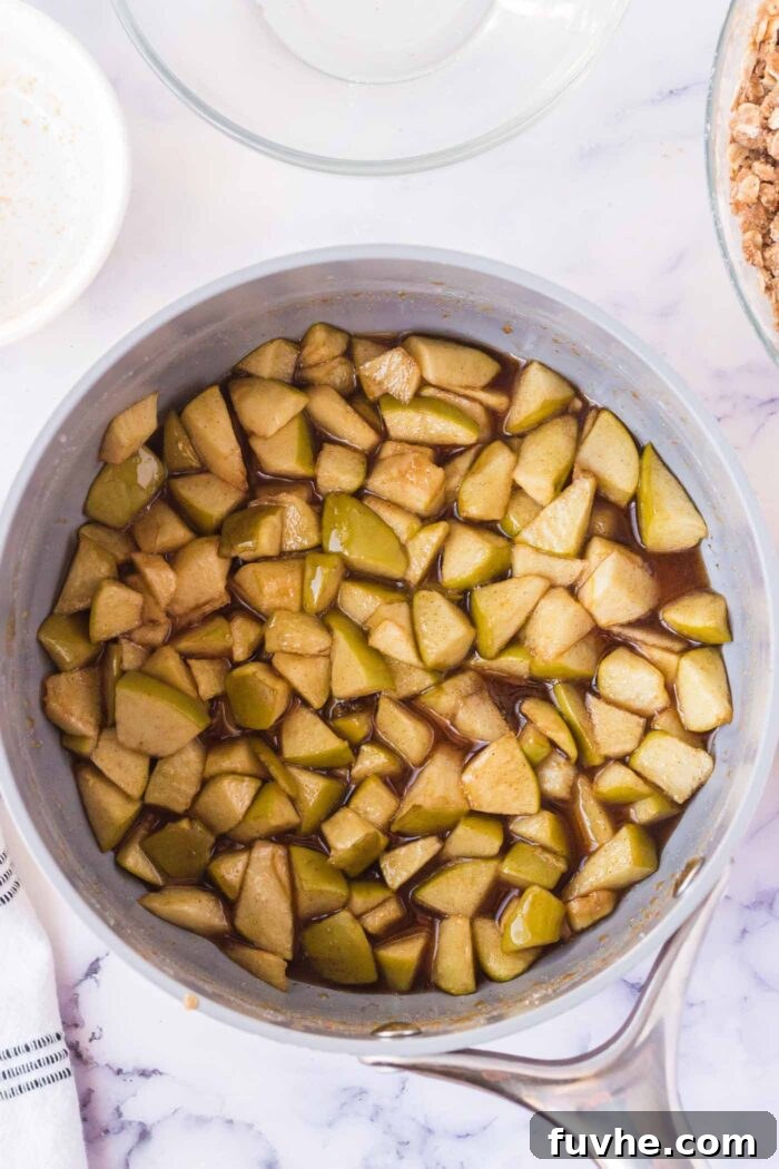 Diced apples gently cooking in a pot on the stove, mingling with lemon juice and aromatic spices to create a fragrant filling.