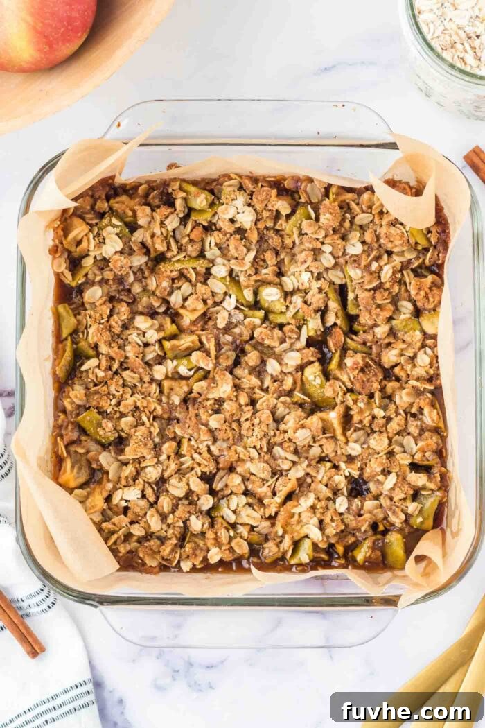 Freshly baked apple crumble bars, golden brown and glistening, cooling in a glass baking dish lined with parchment paper.