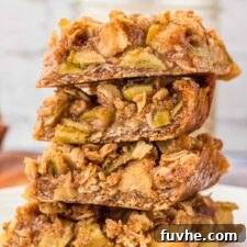 Stack of 4 apple crumble bars on a plate. The bars have an oatmeal crust and crumble topping with a layer of apple pie filling in between.