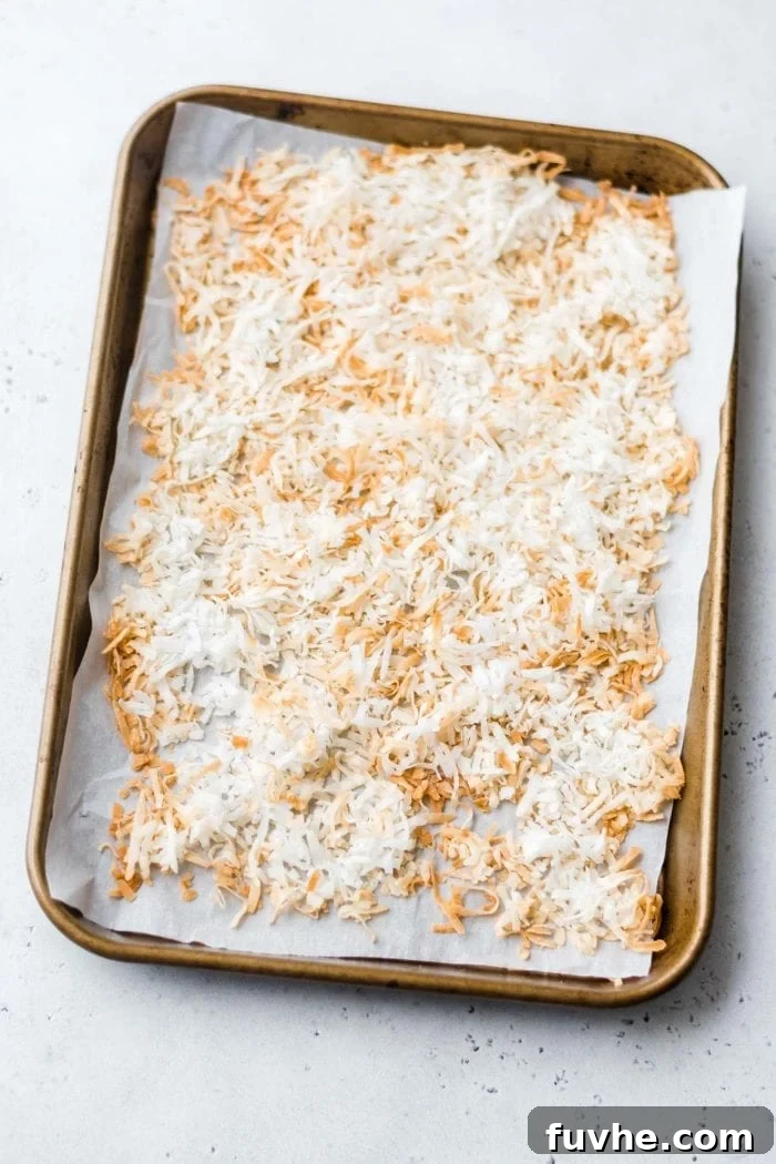 Toasted shredded coconut evenly spread on a baking tray, ready to be incorporated into paleo granola bars.
