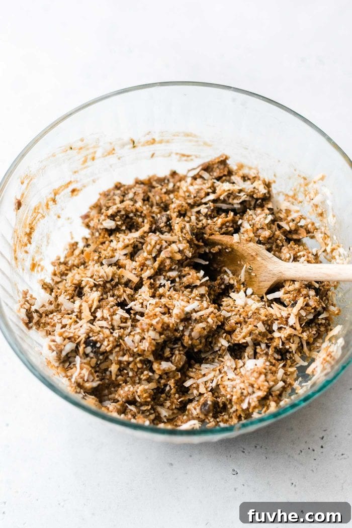A sticky paleo energy bar dough, featuring coconut and nut butter, being mixed in a large bowl.