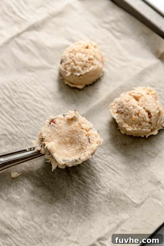 Plant-Powered Almond Coconut Dreams 6 Almond macaroon cookie dough pressed into a small cookie scoop on a baking tray with two almond macaroons beside it.