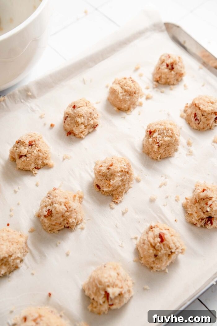 Plant-Powered Almond Coconut Dreams 7 15 small unbaked almond coconut macaroons on a baking tray lined with parchment paper.