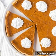Overhead view of a vegan sweet potato pie cut into slices and topped with dollops of whipped cream.