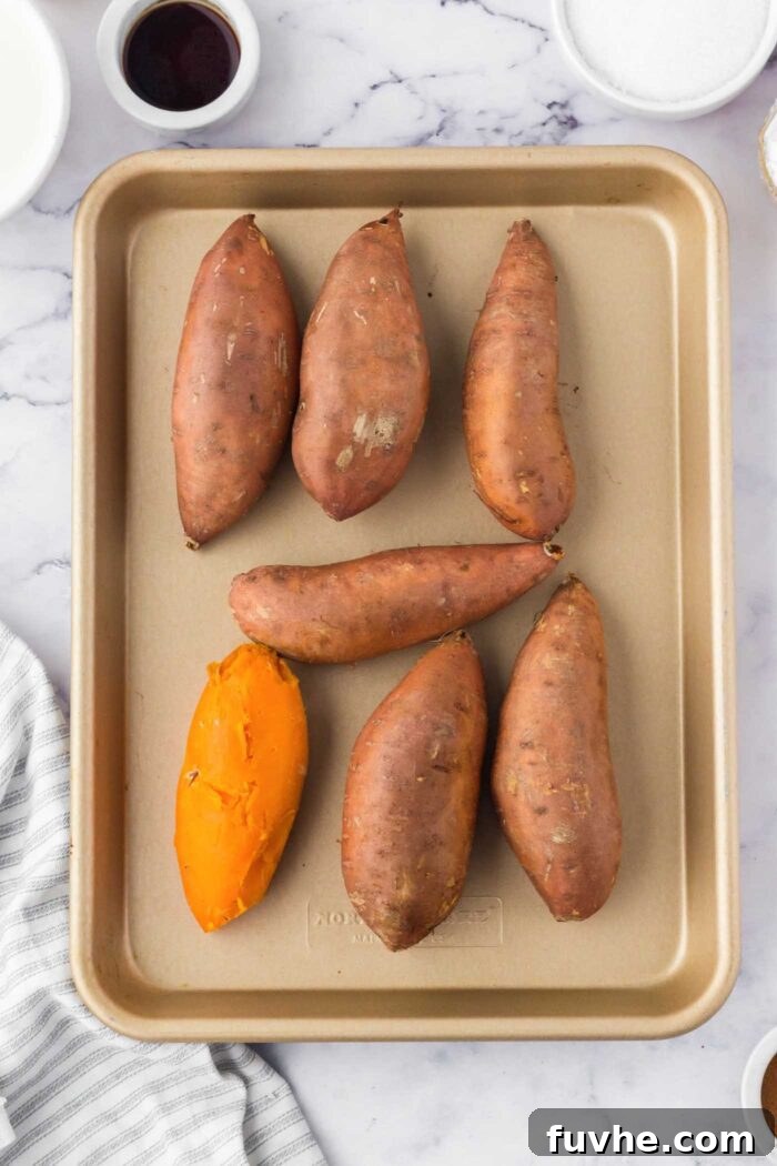 7 baked sweet potatoes on a baking tray. One of them is peeled.