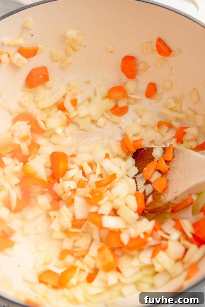 Chopped onion, garlic, ginger and carrot cooking in a large soup pot with a wooden spoon.