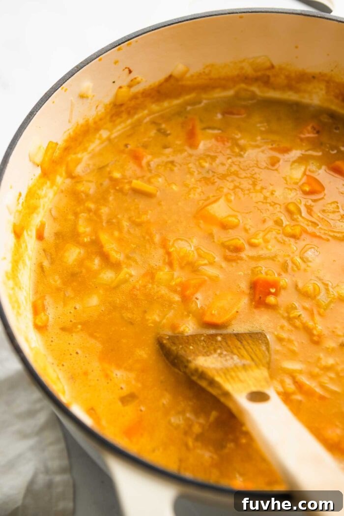 A creamy sweet potato red lentil soup cooking in a large soup pot.