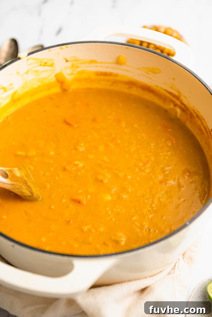 Creamy soup made with sweet potato and red lentils cooking in a pot with a wooden spoon.