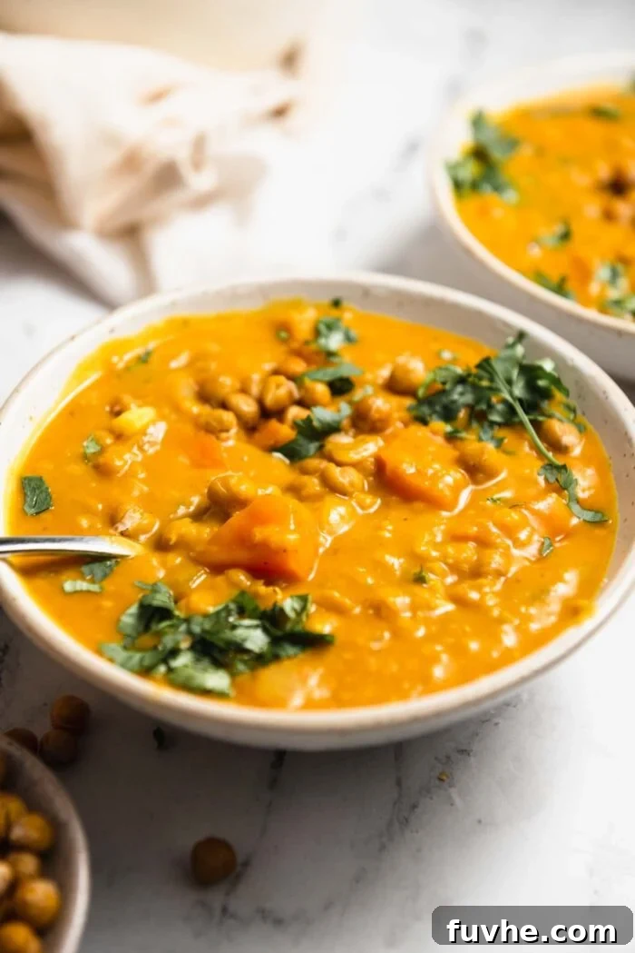 A bowl of sweet potato lentil soup topped with crispy chickpeas and cilantro. A second bowl can be seen in the background.