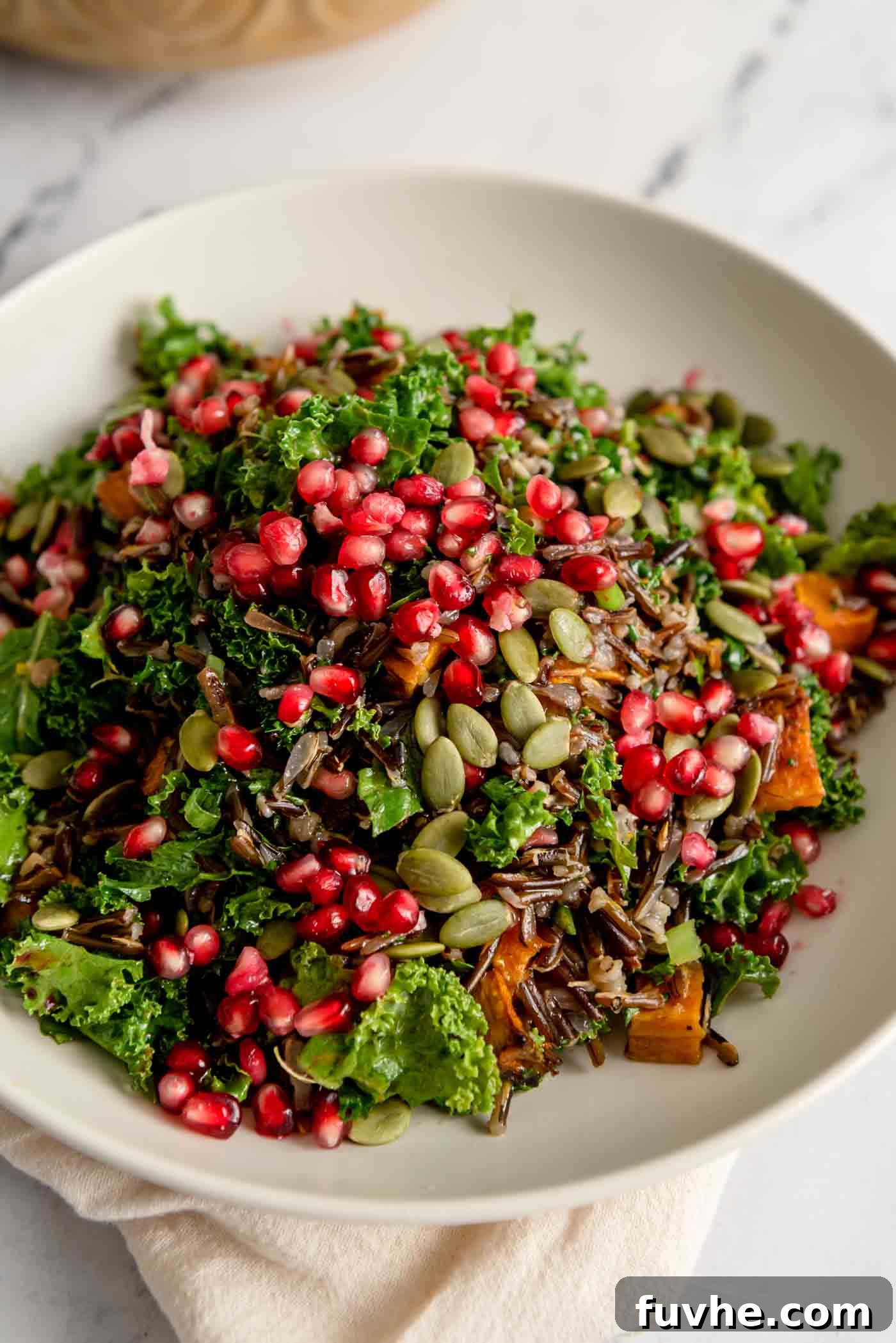 Rustic Wild Rice Salad 2 A bowl of colourful wild rice salad topped with pomegranate arils and pumpkin seeds, showcasing vibrant ingredients.