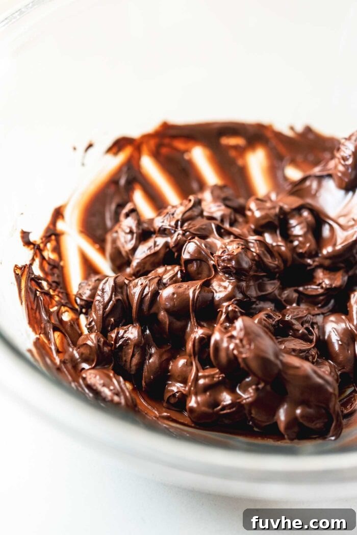 Irresistible Nutty Clusters 5 A delectable mixture of almonds and vibrant dried cranberries coated generously in melted chocolate within a clear glass mixing bowl, ready to be formed into clusters.