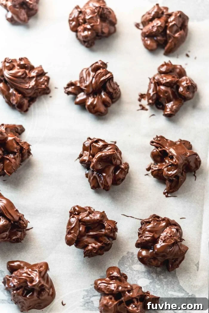 Irresistible Nutty Clusters 6 A pristine parchment paper-lined baking sheet showcasing freshly formed chocolate nut clusters. The chocolate is still liquid, indicating they are awaiting chilling.