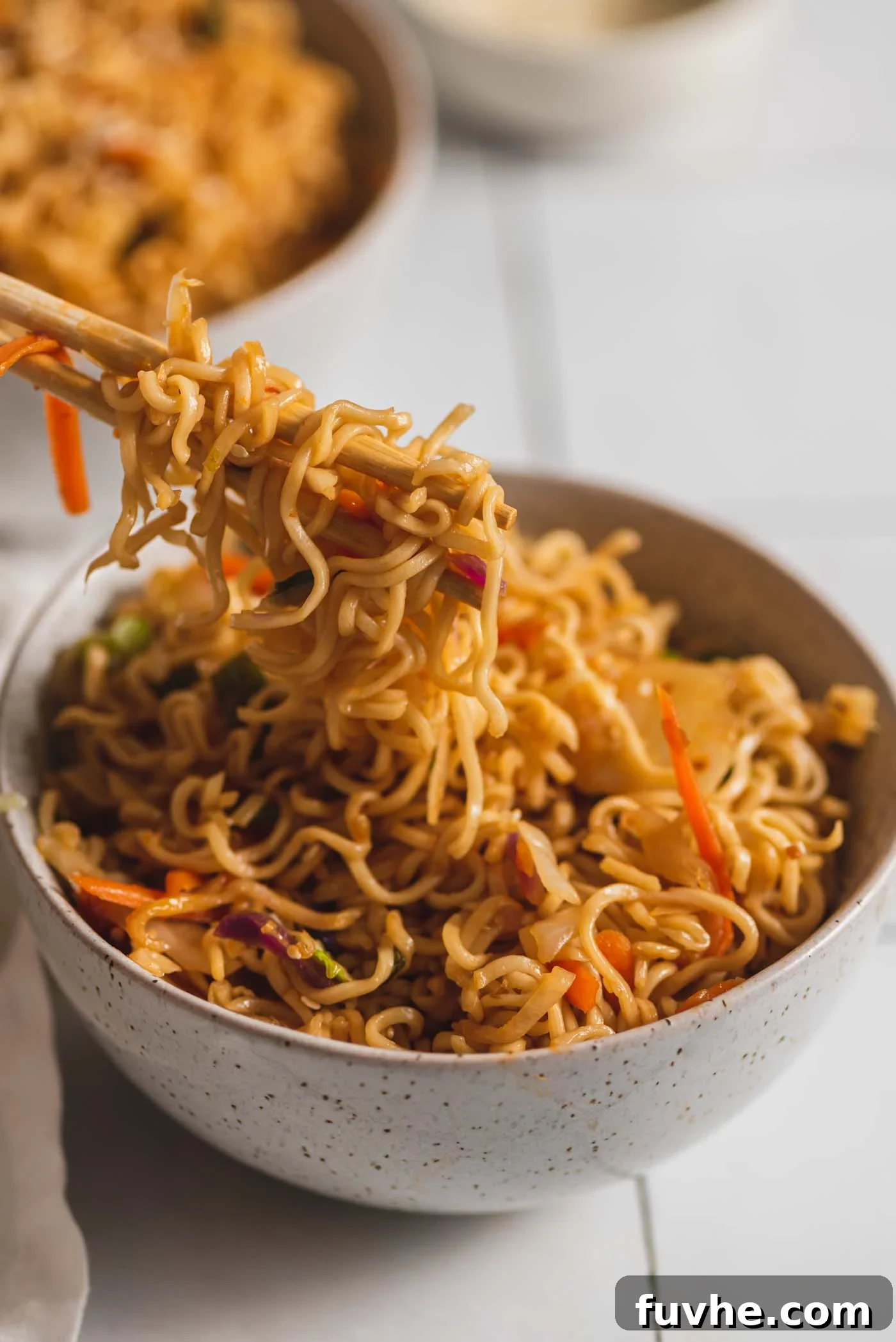 Chopsticks being used in a small bowl of vegetarian pan fried ramen noodles with cabbage.