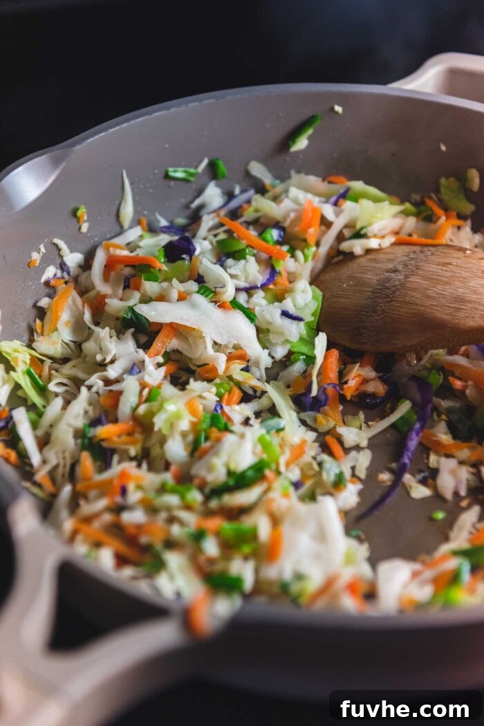 Stir fried cabbage, julienned carrot and green onion cooking in a skillet with a wooden spoon in the skillet.