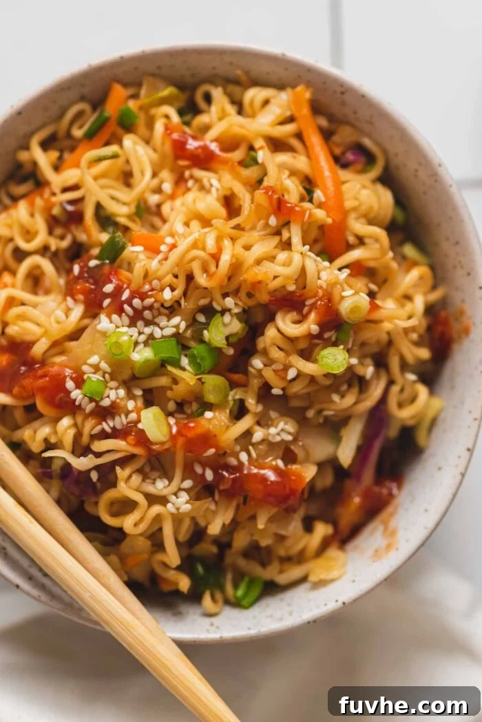 Overhead view of a bowl of pan fried ramen noodles with vegetables topped with sesame seeds and green onion.