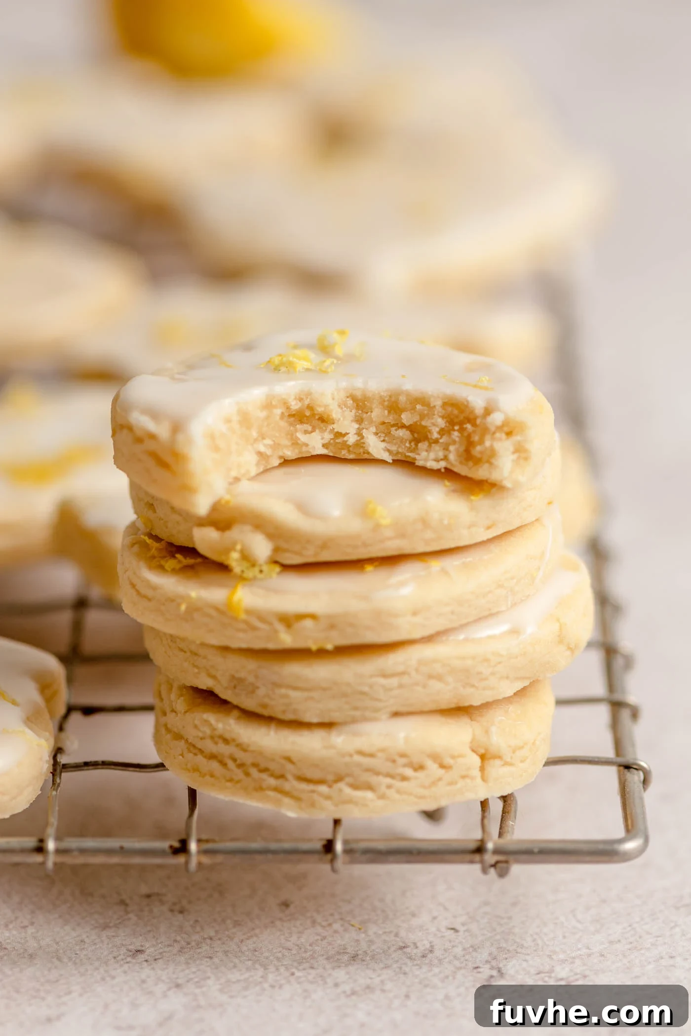 Zesty Lemon Shortbread Bites 2 A stack of small, round lemon shortbread cookies with icing on a cooling rack. The cookie on top has a bite out of it.